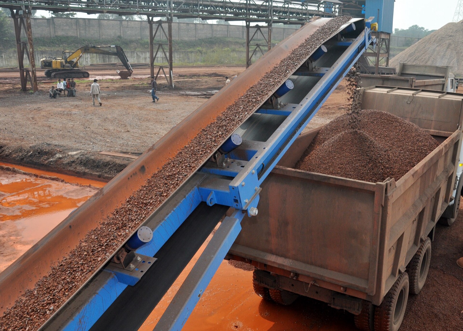 Conveyor loading ore into a truck beside a stockpile